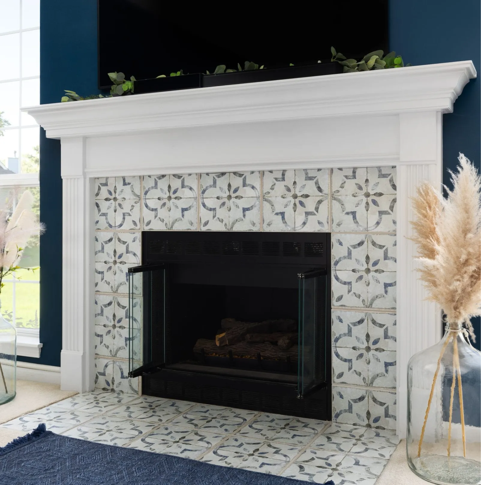 fireplace-1 White fireplace with patterned tile surround, glass doors, pampas grass in vases, and plants on the mantel.