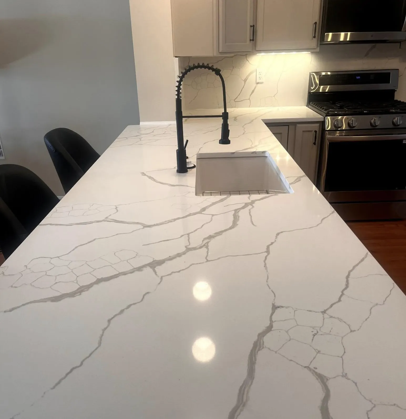services-1 White marble kitchen island with grey veining, black faucet, and a built-in sink under bright lighting.