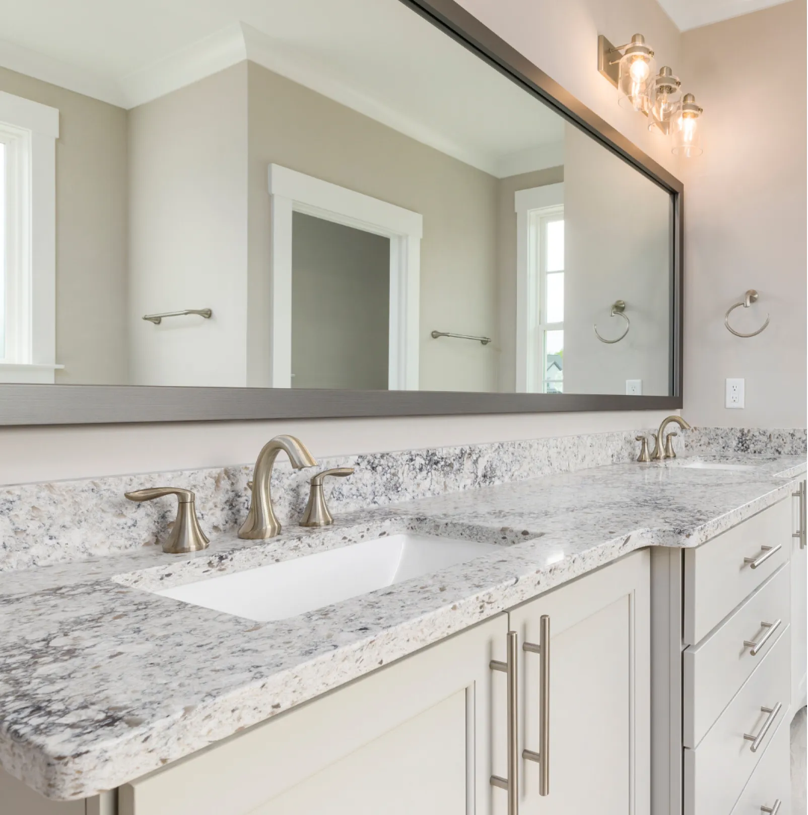 vanity-1 (1) Modern bathroom with a granite double sink vanity, brushed nickel fixtures, and a large wall mirror.