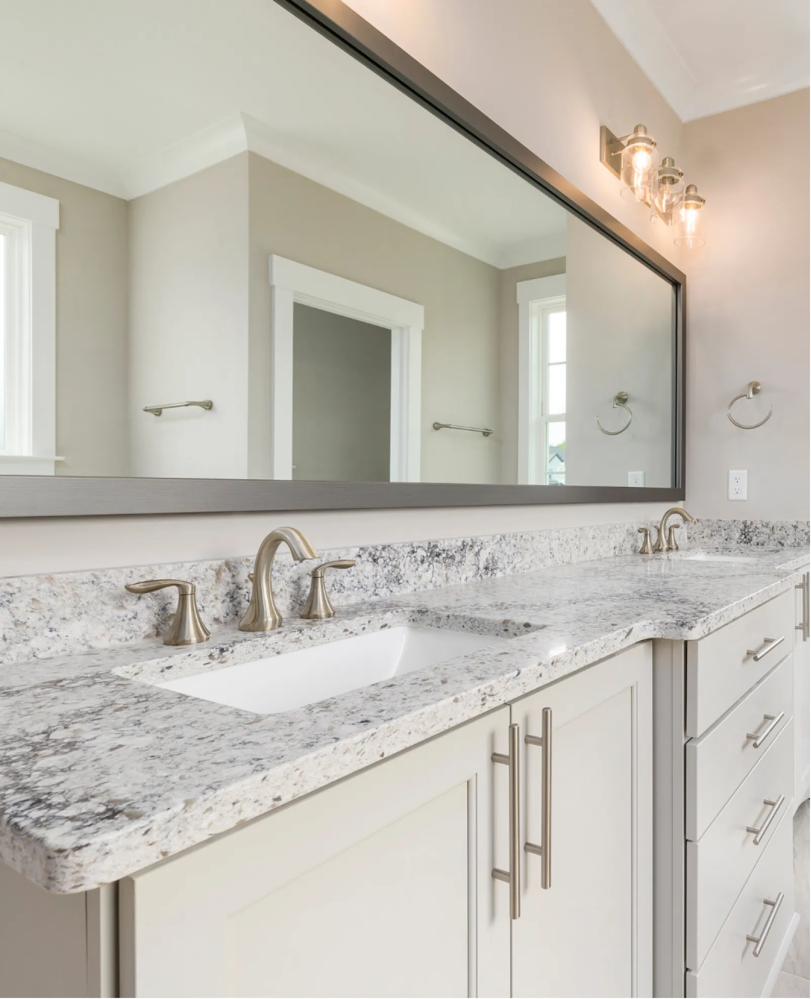 vanity-1 Modern bathroom with granite countertop, double sinks, chrome faucets, large mirror, and neutral walls.